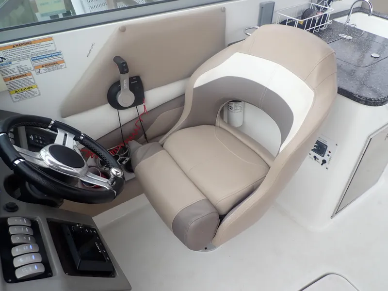 Slide: The Image of 2016 Hurricane SunDeck 2690 OB boat interior with steering wheel and beige captain's chair. - 12