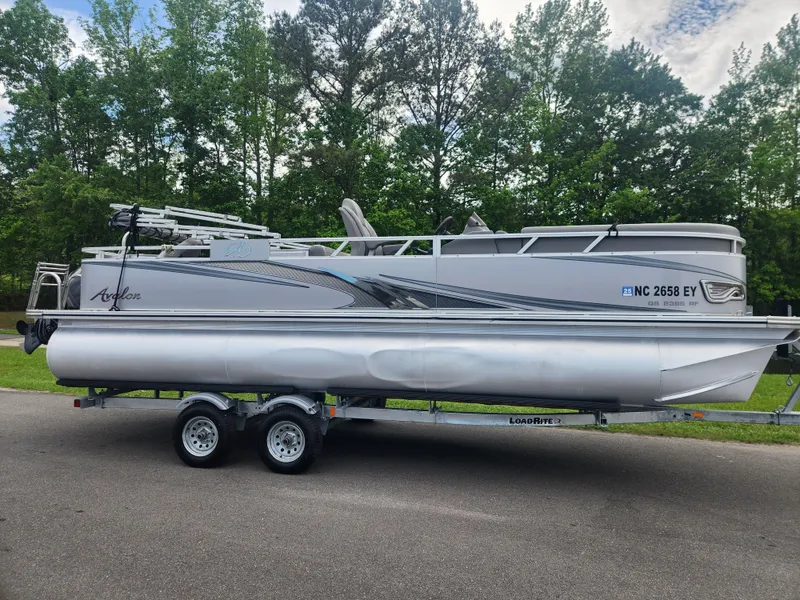 Slide: The Image of 2022 Avalon GS RF 2385 pontoon boat on trailer, parked on road with trees in background. - 0