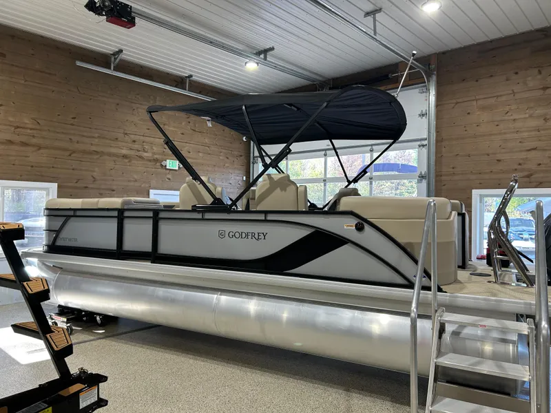 Slide: The Image of 2025 Godfrey Sweetwater 2286 QS pontoon boat in showroom, featuring sleek design and canopy. - 2