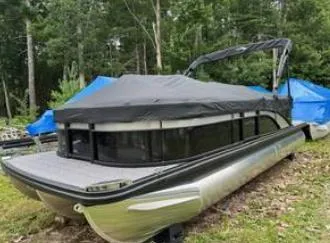 Slide: The Image of 2025 Bennington 22 SXSR pontoon boat with cover, parked outdoors in a wooded area. - 13