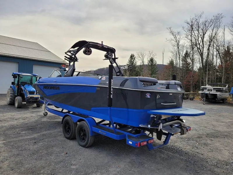 Slide: The Image of 2022 Moomba Makai boat on trailer, blue and black, parked outdoors near a tractor. - 3