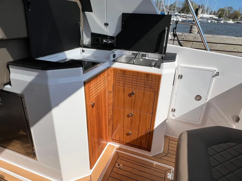 Slide: The Image of 2024 Aquador 250 HT boat interior with kitchenette, featuring wood cabinetry and compact sink. - 12