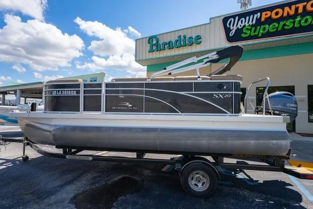 Slide: The Image of 2019 Bennington 20 SX pontoon boat on trailer at dealership under blue sky. - 2
