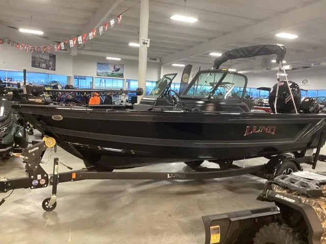 Slide: The Image of 2025 Lund 1875 Impact XS boat displayed in a showroom, featuring sleek black design. - 2