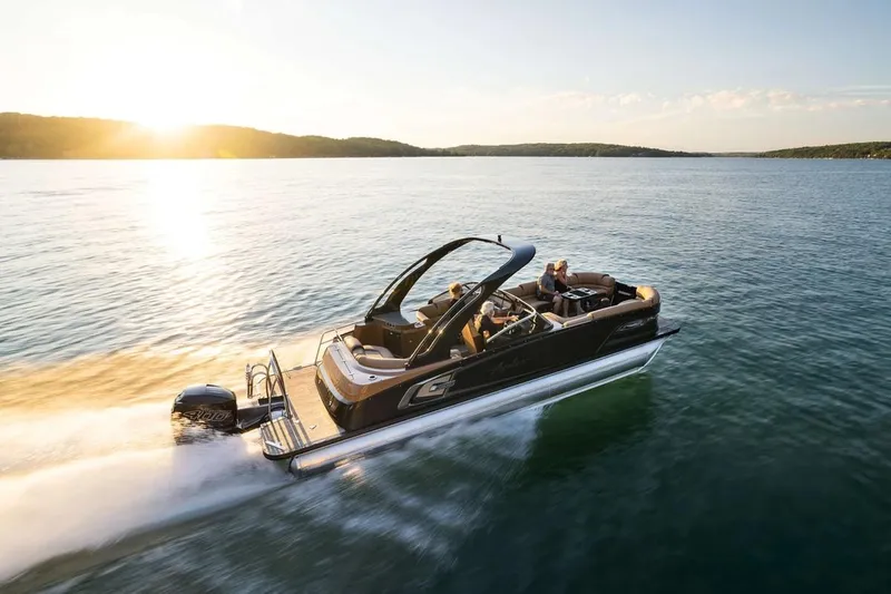 Slide: The Image of 2024 Avalon Excalibur LTD Elite Windshield boat cruising on a serene lake at sunset. - 3