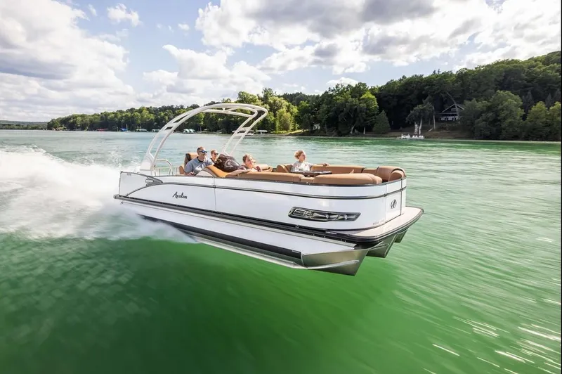 Slide: The Image of 2024 Avalon Excalibur LTD Elite Windshield boat cruising on a scenic lake. - 7