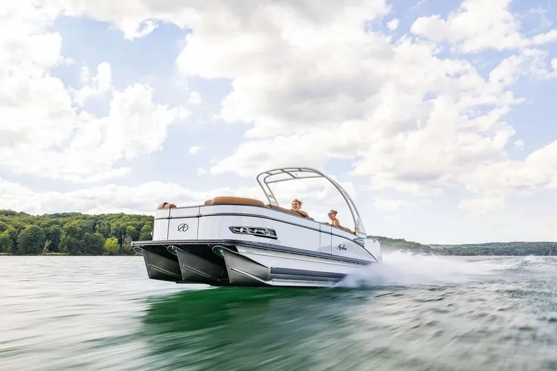Slide: The Image of 2024 Avalon Excalibur LTD Elite Windshield boat cruising on a lake under a cloudy sky. - 8