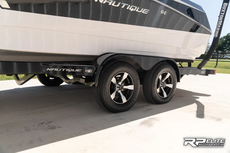 Slide: The Image of 2014 Nautique Super Air Nautique 230 boat on trailer, featuring dual axles and stylish wheels. - 21