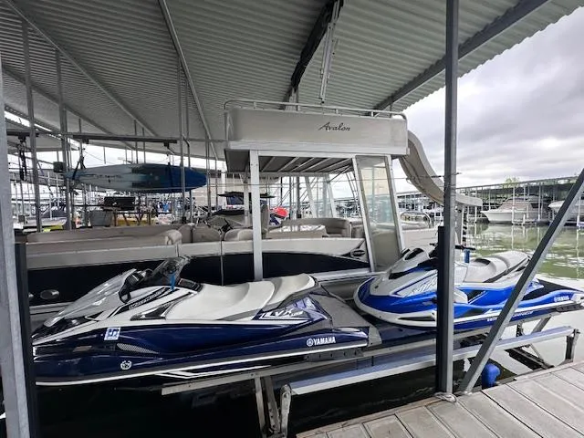 Slide: The Image of 2016 Tahoe Pontoon Vista Funship Entertainer with jet skis docked under a covered marina. - 2