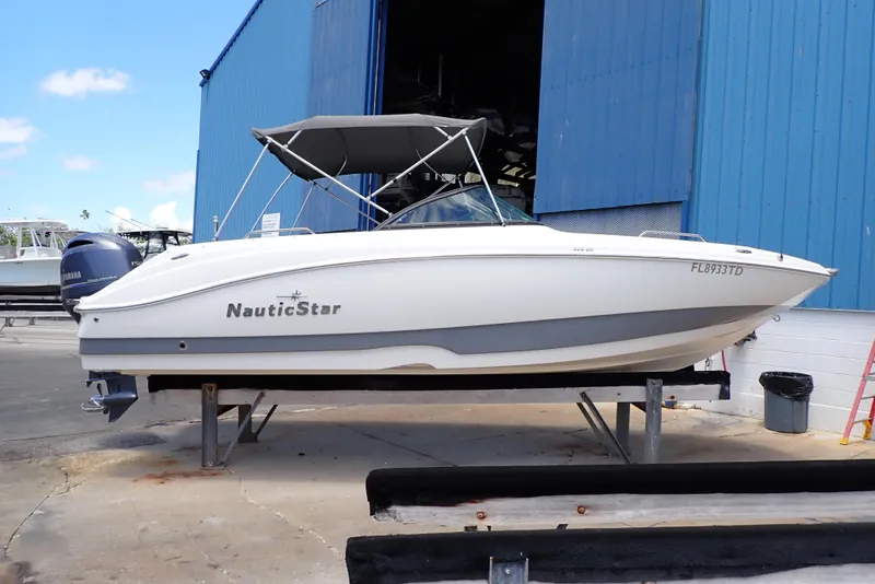 Slide: The Image of 2021 NauticStar 223 DC boat on display outside a blue building. - 0