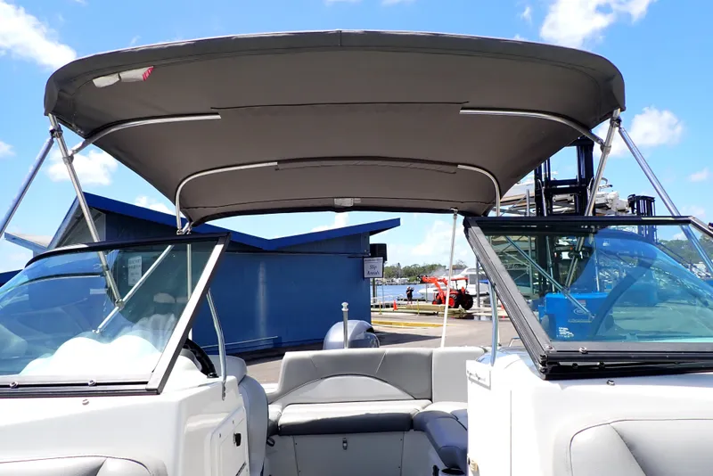 Slide: The Image of 2021 NauticStar 223 DC boat with bimini top, docked under clear blue sky. - 22