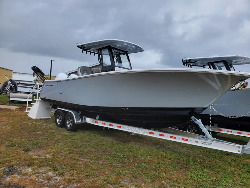 Slide: The Image of 2025 Sportsman Heritage 261 Center Console boat on trailer, parked on grass under cloudy sky. - 0