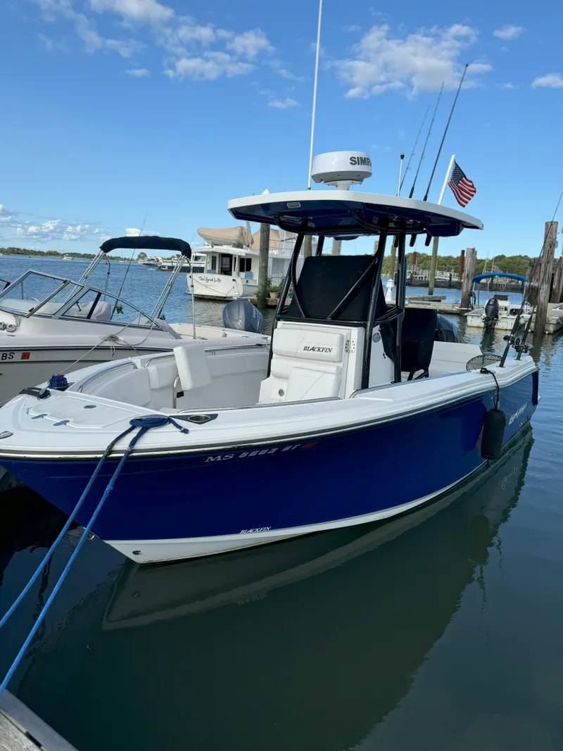 Slide: The Image of 2020 Blackfin 212 CC boat docked, blue hull, clear sky, American flag, fishing rods visible. - 49