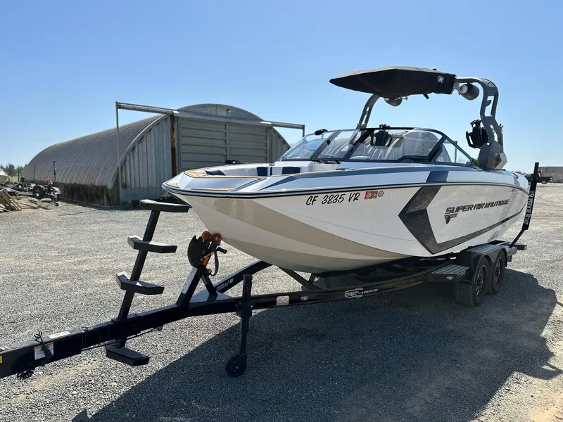 Slide: The Image of 2019 Nautique Super Air G23 boat on trailer, parked outdoors near a metal building. - 3