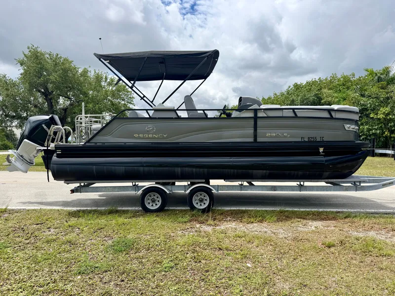 Slide: The Image of 2022 Regency 230 LE3 pontoon boat on trailer, parked outdoors under cloudy sky. - 5