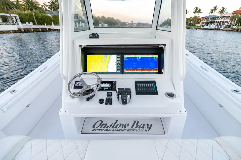 Slide: The Image of 2022 Onslow Bay 41 TE boat dashboard with navigation screens and steering wheel on a calm waterway. - 14