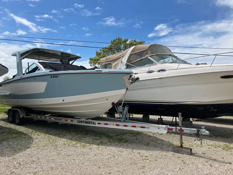 Slide: The Image of 2022 Aviara AV32 OB boat on trailer, parked beside another boat, under a clear blue sky. - 2