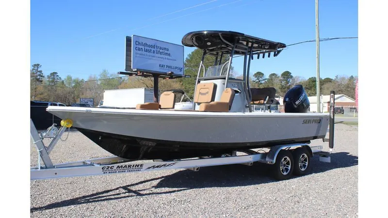 Slide: The Image of 2025 Sea Pro 230 Bay boat on trailer, parked outdoors, with trees and billboard in background. - 4