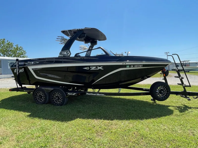 Slide: The Image of 2021 Tigé 23ZX boat on trailer, black exterior, parked on grass under clear blue sky. - 0