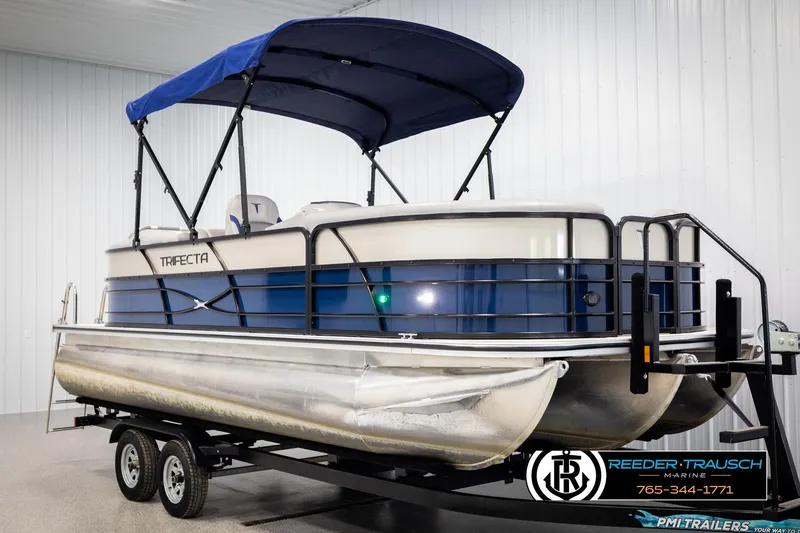 Slide: The Image of 2021 Trifecta 22 CS pontoon boat with blue canopy on trailer in showroom. - 2