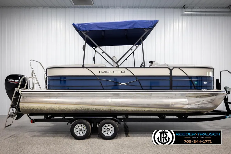 Slide: The Image of 2021 Trifecta 22 CS pontoon boat with blue canopy on trailer in showroom. - 4