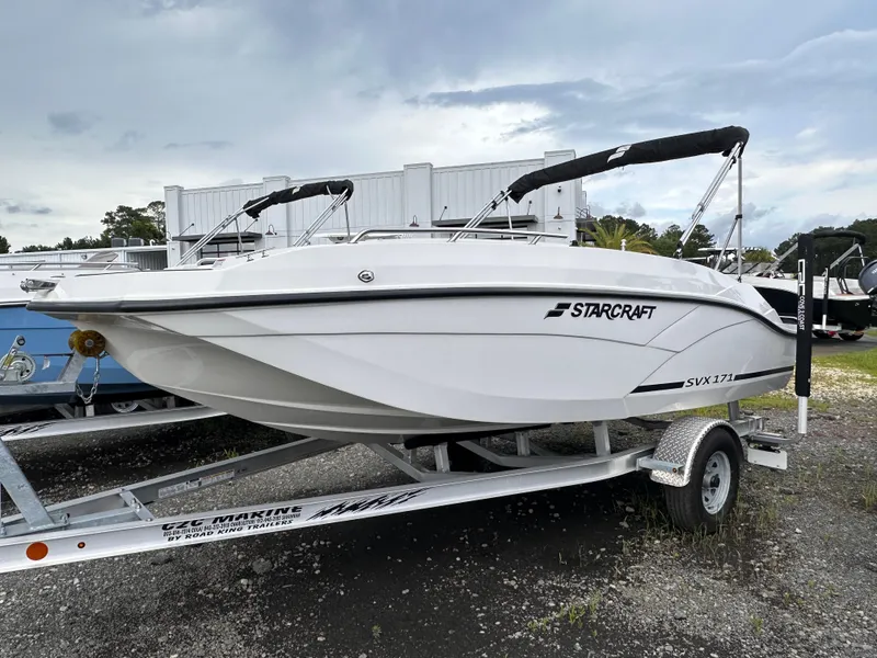 Slide: The Image of 2024 Starcraft 171 SVX boat on trailer, white exterior, parked outdoors under cloudy sky. - 2
