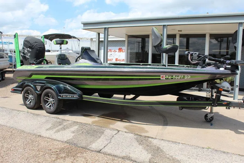 Slide: The Image of 2017 Skeeter FX20 LE bass boat with green accents on a trailer, parked outside a dealership. - 0