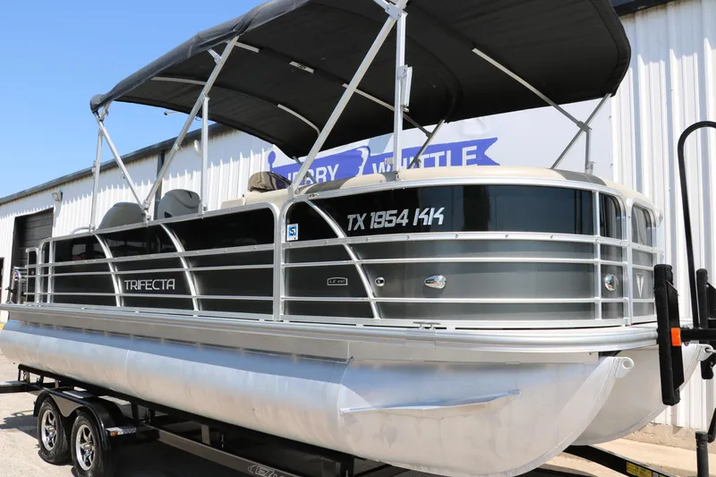 Slide: The Image of 2021 Trifecta 24 RFC pontoon boat on trailer, black canopy, parked outside a building. - 9