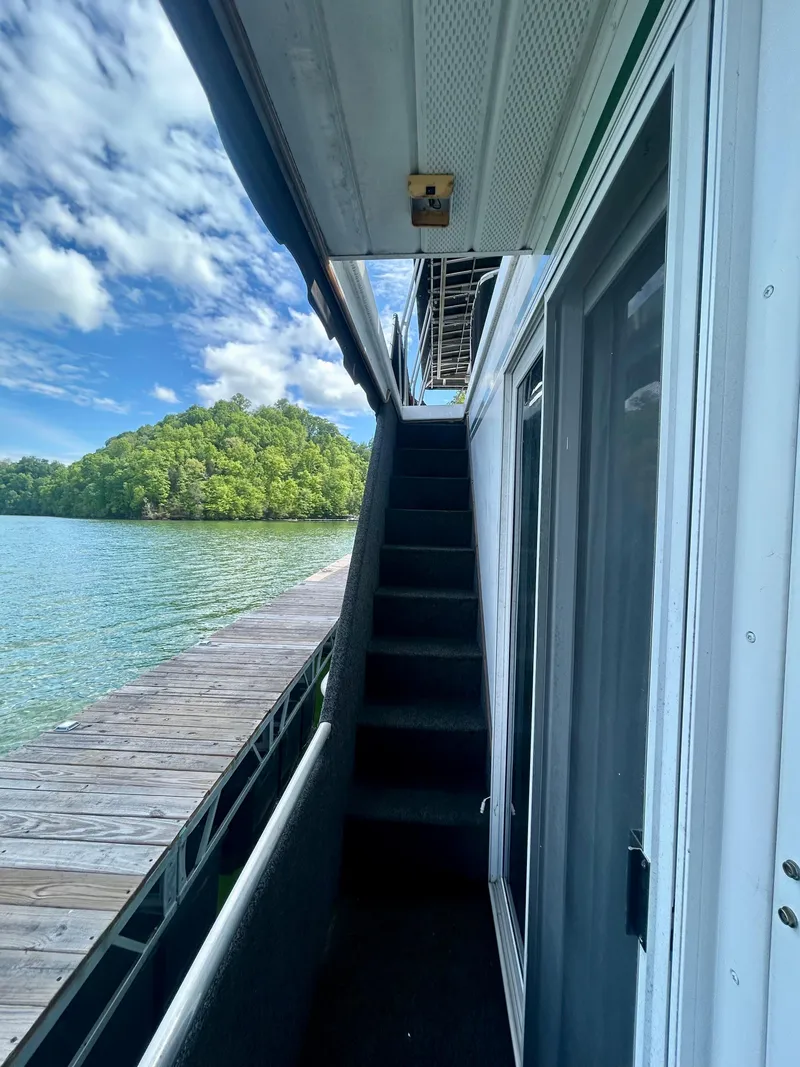Slide: The Image of 2002 Sumerset houseboat with exterior stairs, docked by a scenic lake and lush greenery. - 6