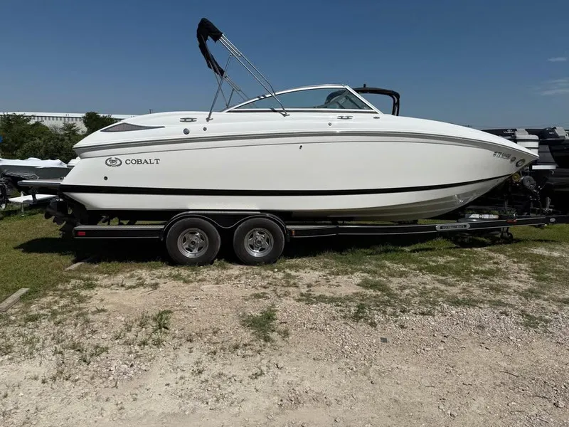 Slide: The Image of 2012 Cobalt 242 boat on trailer, parked on grass under clear blue sky. - 0