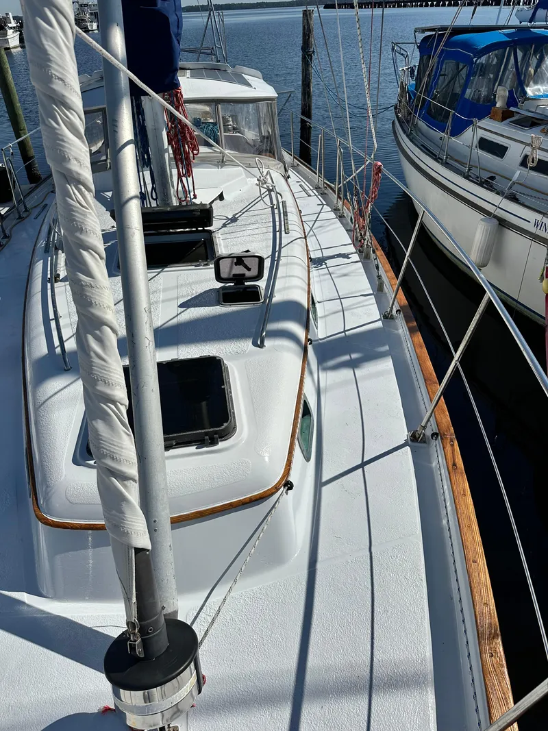 Slide: The Image of 1981 Kelly Peterson 44 sailboat deck, docked beside another vessel, under clear skies. - 10