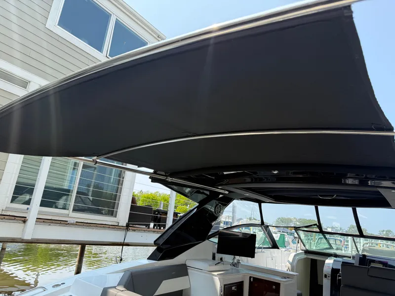 Slide: The Image of 2021 Cruisers Yachts 38 GLS OB with black canopy, docked near modern building. - 12