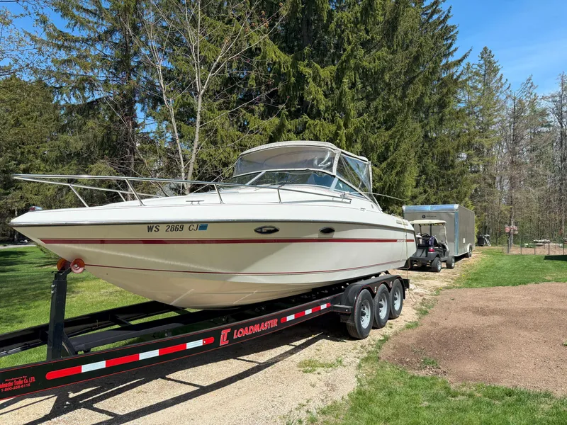 The Image of 1988 Slickcraft 268 SC boat on trailer, parked outdoors with trees in background. - 0