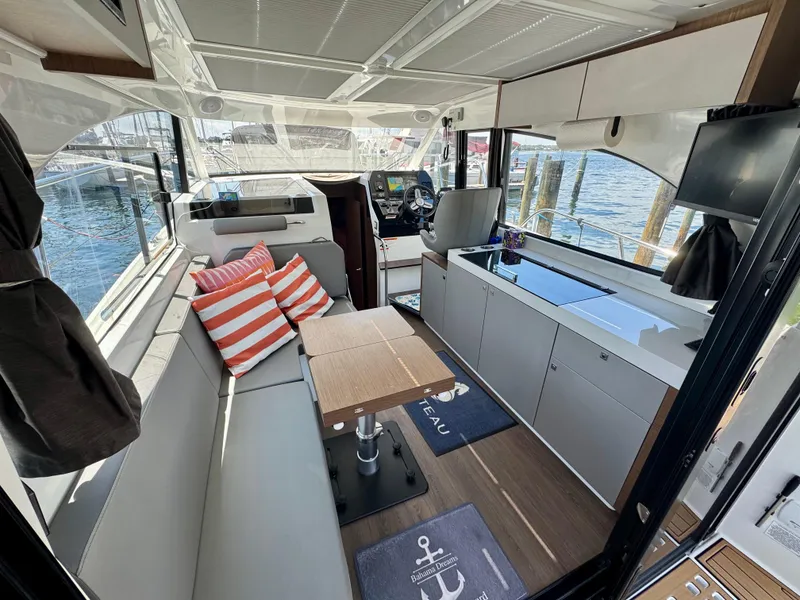 Slide: The Image of 2024 Beneteau Antares 11 interior with seating, table, and helm, overlooking marina. - 14
