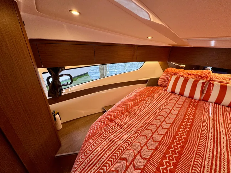 Slide: The Image of 2024 Beneteau Antares 11 cabin with red patterned bedding and modern wood finish. - 23