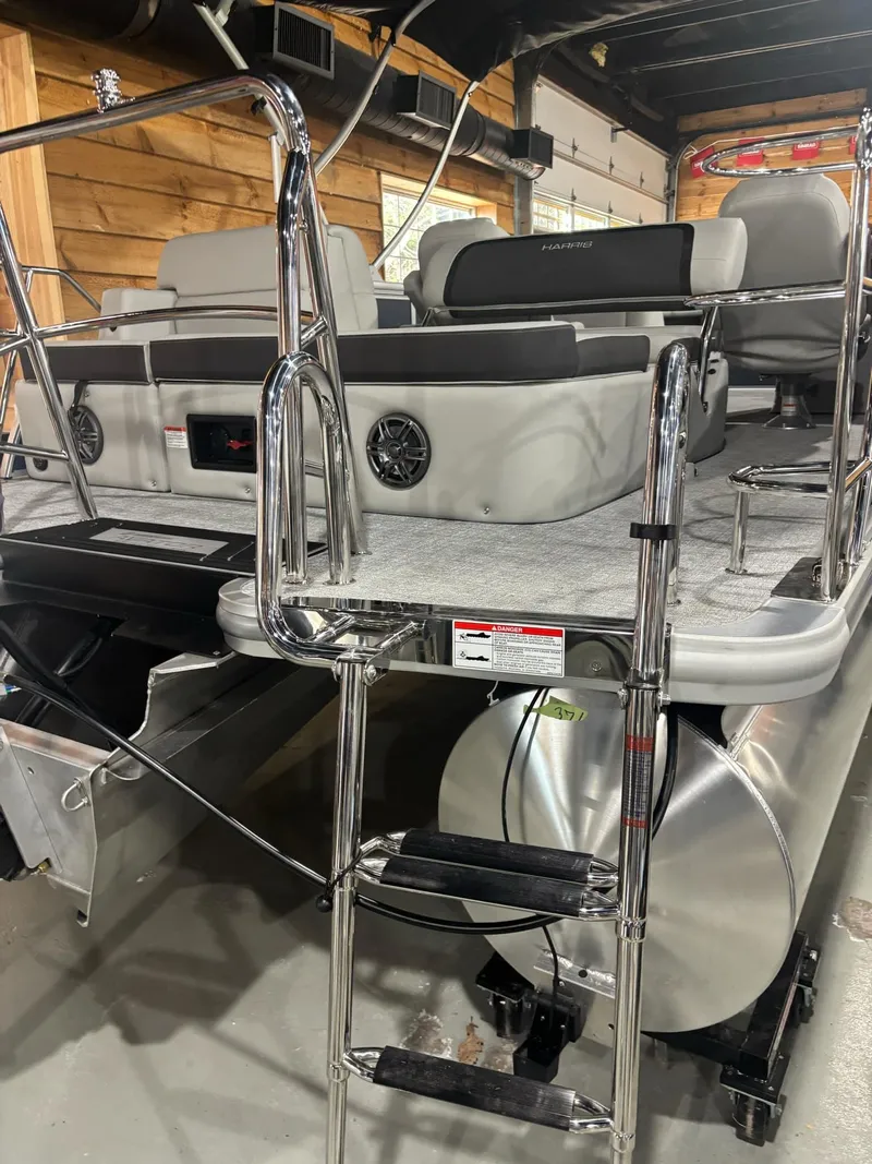 Slide: The Image of 2025 Harris Cruiser 210 pontoon boat with chrome ladder and plush seating in a wooden interior setting. - 16