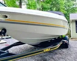 Slide: The Image of 2000 Baja 232 Islander boat on trailer, parked outdoors near trees and a house. - 2