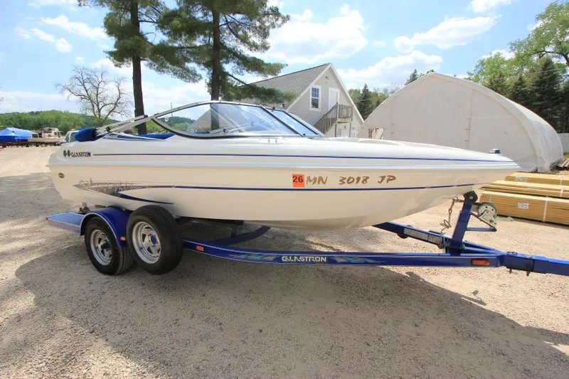 Slide: The Image of 2003 Glastron SX 175 boat on trailer, parked outdoors near trees and buildings. - 1