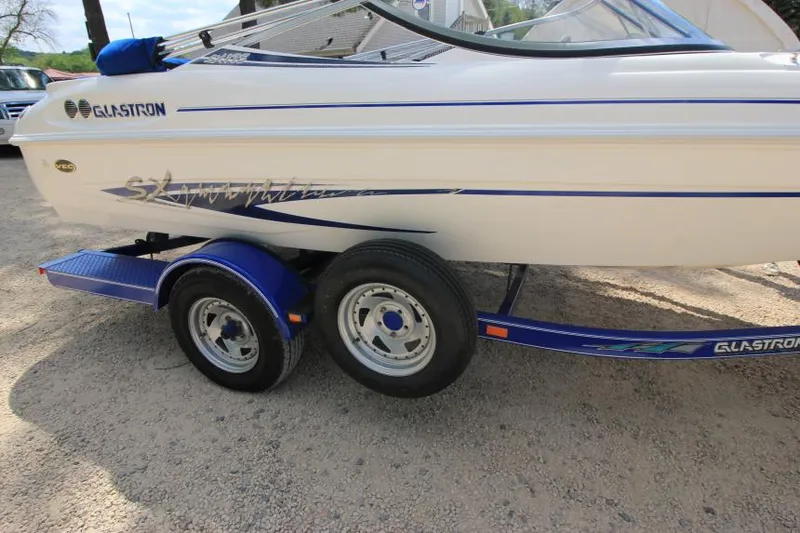 Slide: The Image of 2003 Glastron SX 175 boat on a blue trailer, parked on gravel. - 6