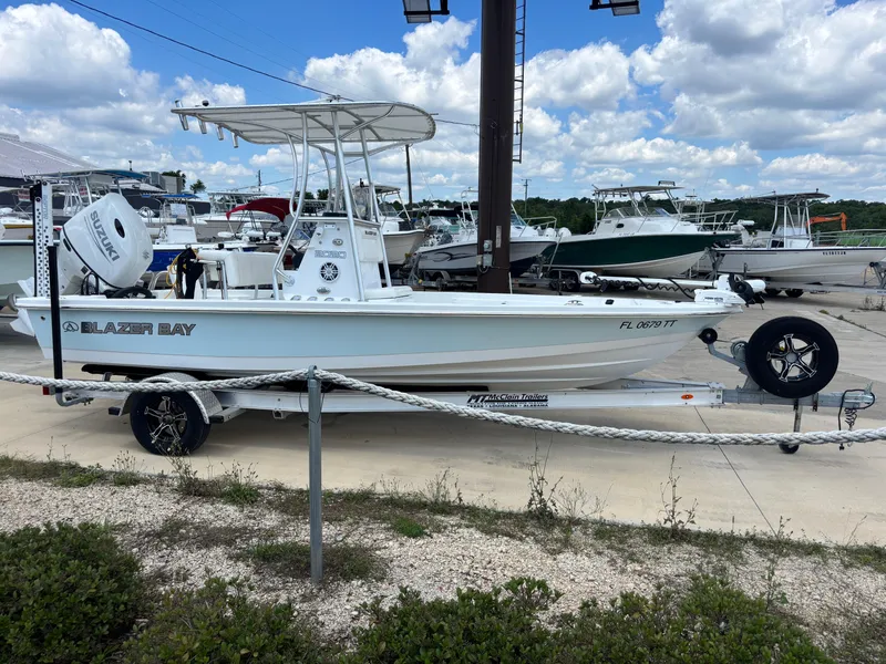 Slide: The Image of 2023 Blazer Bay boat on trailer at marina, under a partly cloudy sky. - 2