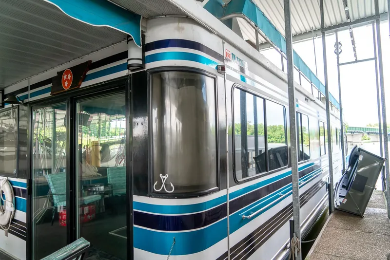 Slide: The Image of 1991 Sumerset 65 x 14 Widebody Houseboat with blue and white exterior docked under a canopy. - 35