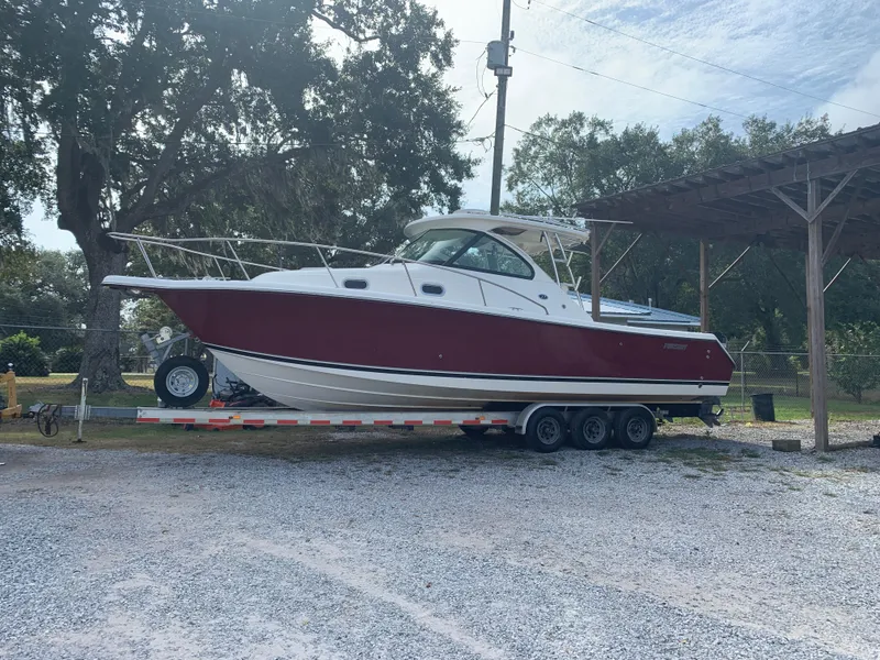 Slide: The Image of 2008 Pursuit 315 OS boat on trailer, parked outdoors under trees. - 6