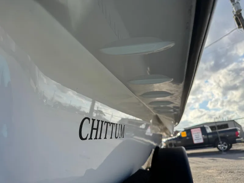 Slide: The Image of 2024 Chittum Skiffs 21 Mangrove boat close-up with logo, parked outdoors. - 22