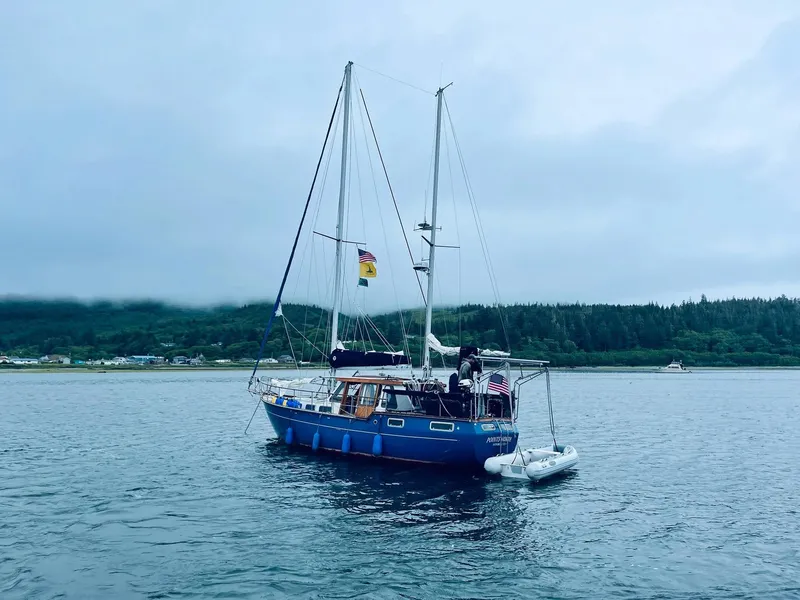 The Image of 1982 Nauticat 38 sailboat anchored on calm water with forested shoreline in the background. - 0