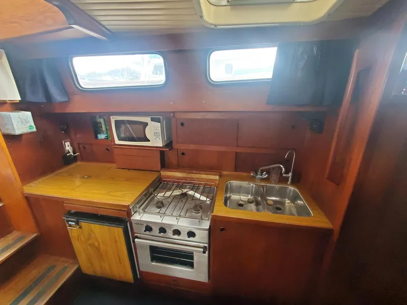 Slide: The Image of 1982 Nauticat 38 yacht kitchen with stove, sink, microwave, and wooden cabinetry. - 2