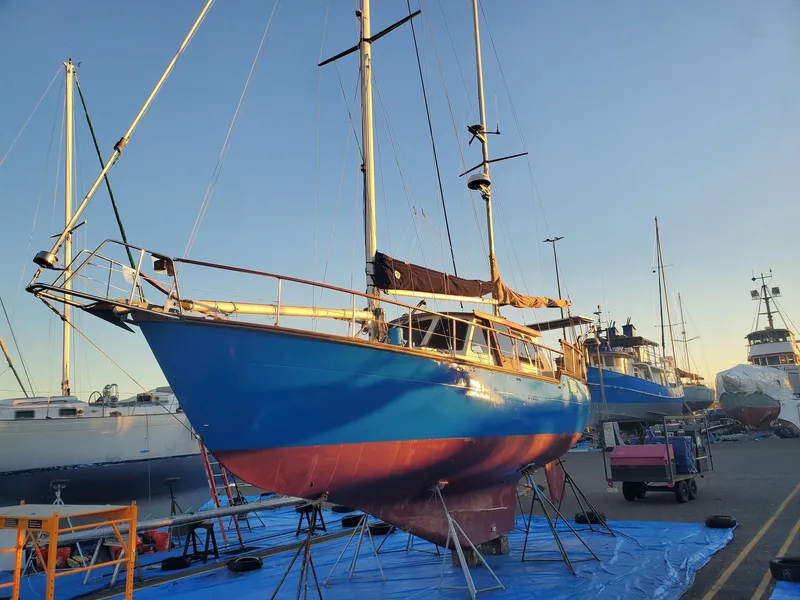 Slide: The Image of 1982 Nauticat 38 sailboat on dry dock, blue hull, masts up, clear sky background. - 9