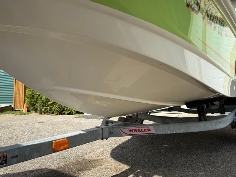 Slide: The Image of 2009 Boston Whaler 130 Super Sport on trailer, green and white hull, parked outdoors. - 6