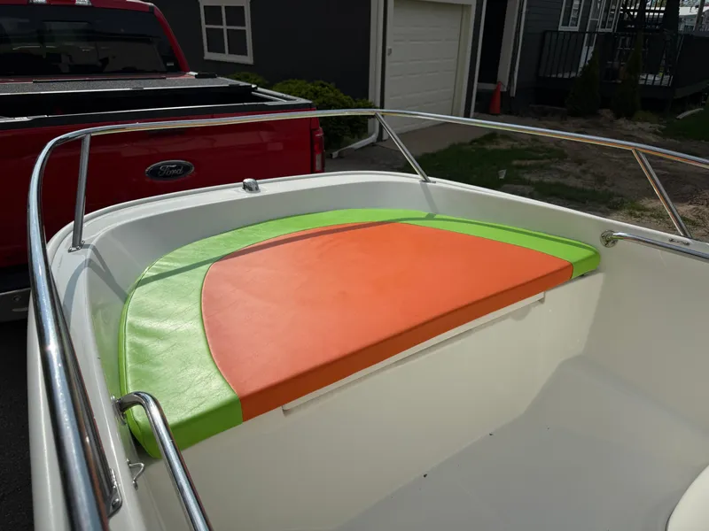 Slide: The Image of 2009 Boston Whaler 130 Super Sport with vibrant orange and green seating, parked near a red truck. - 8