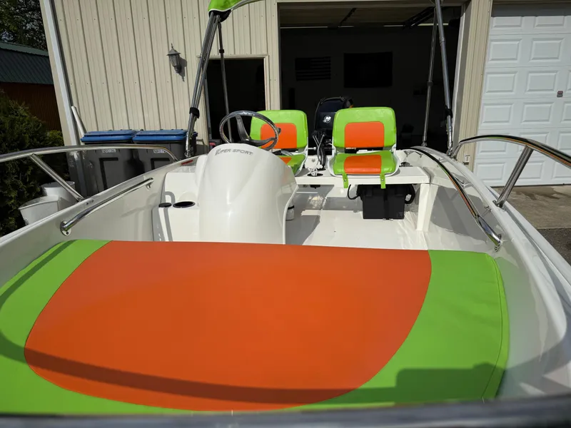 Slide: The Image of 2009 Boston Whaler 130 Super Sport with vibrant green and orange seating in a garage setting. - 9