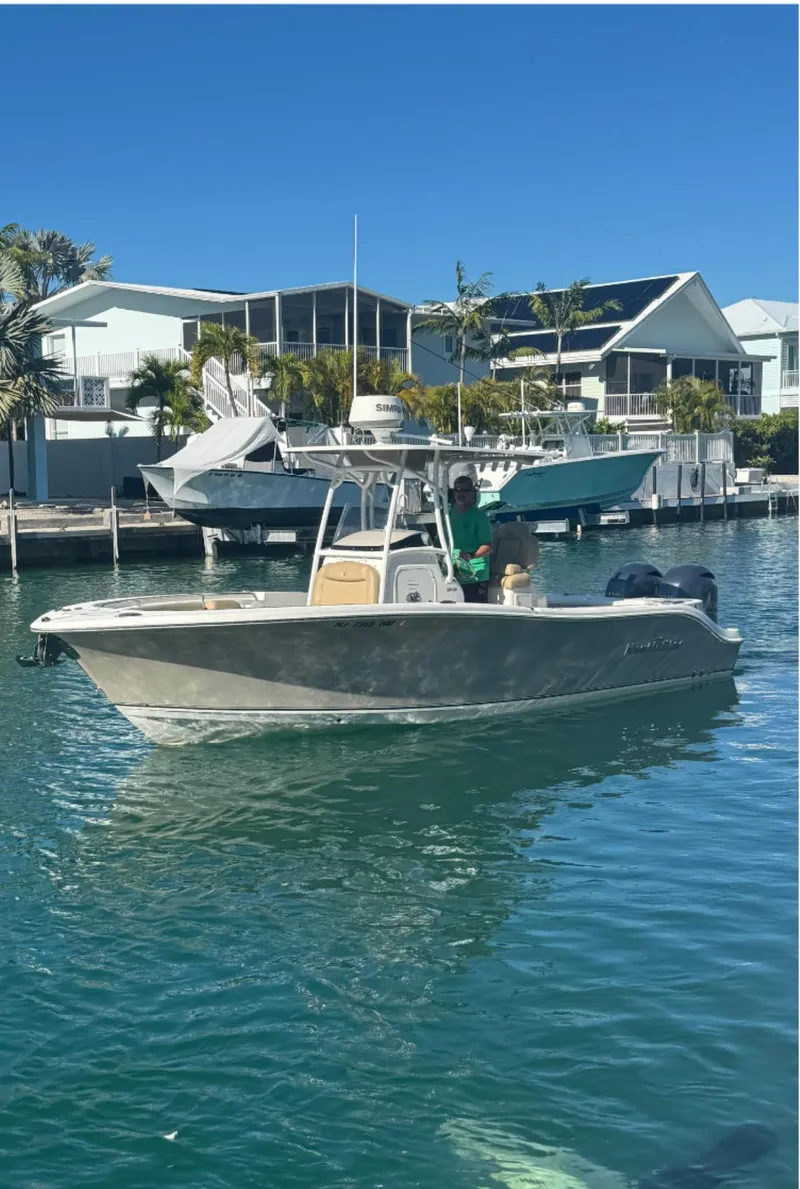 Slide: The Image of 2018 NauticStar 25 XS Offshore boat on calm water near waterfront homes. - 8